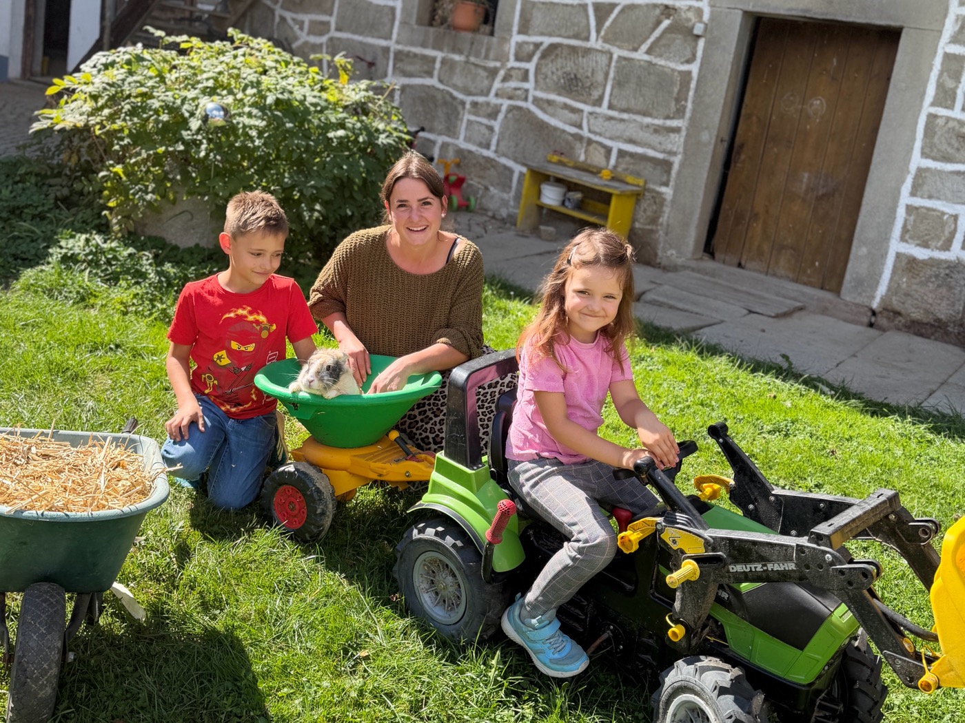 Kinder mit Schubkarre und Spieltraktor im Hof